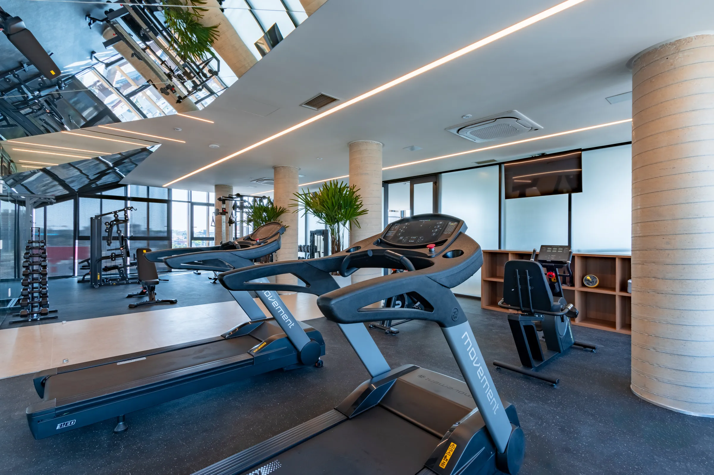 Academia do Vaz Batel com esteiras Movement, aparelhos de musculação, rack de halteres, colunas em concreto aparente e janelas panorâmicas com vista do Batel