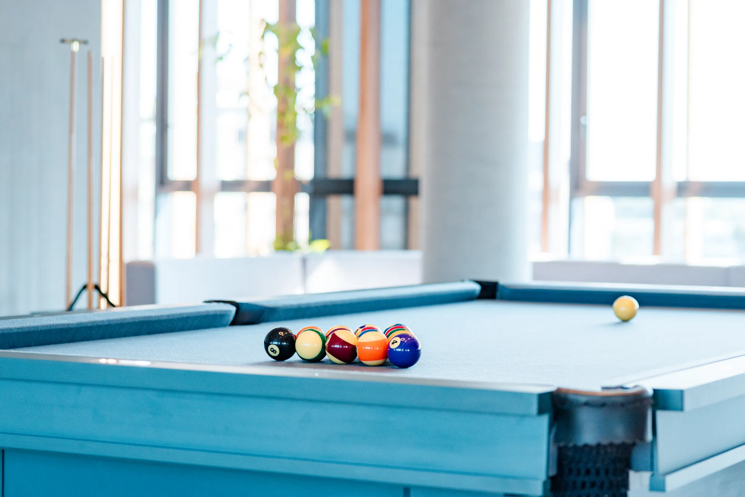 Sala de jogos do Vaz Batel com mesa de bilhar em feltro azul claro, bolas coloridas posicionadas para partida, tacos apoiados e janelas verticais ao fundo