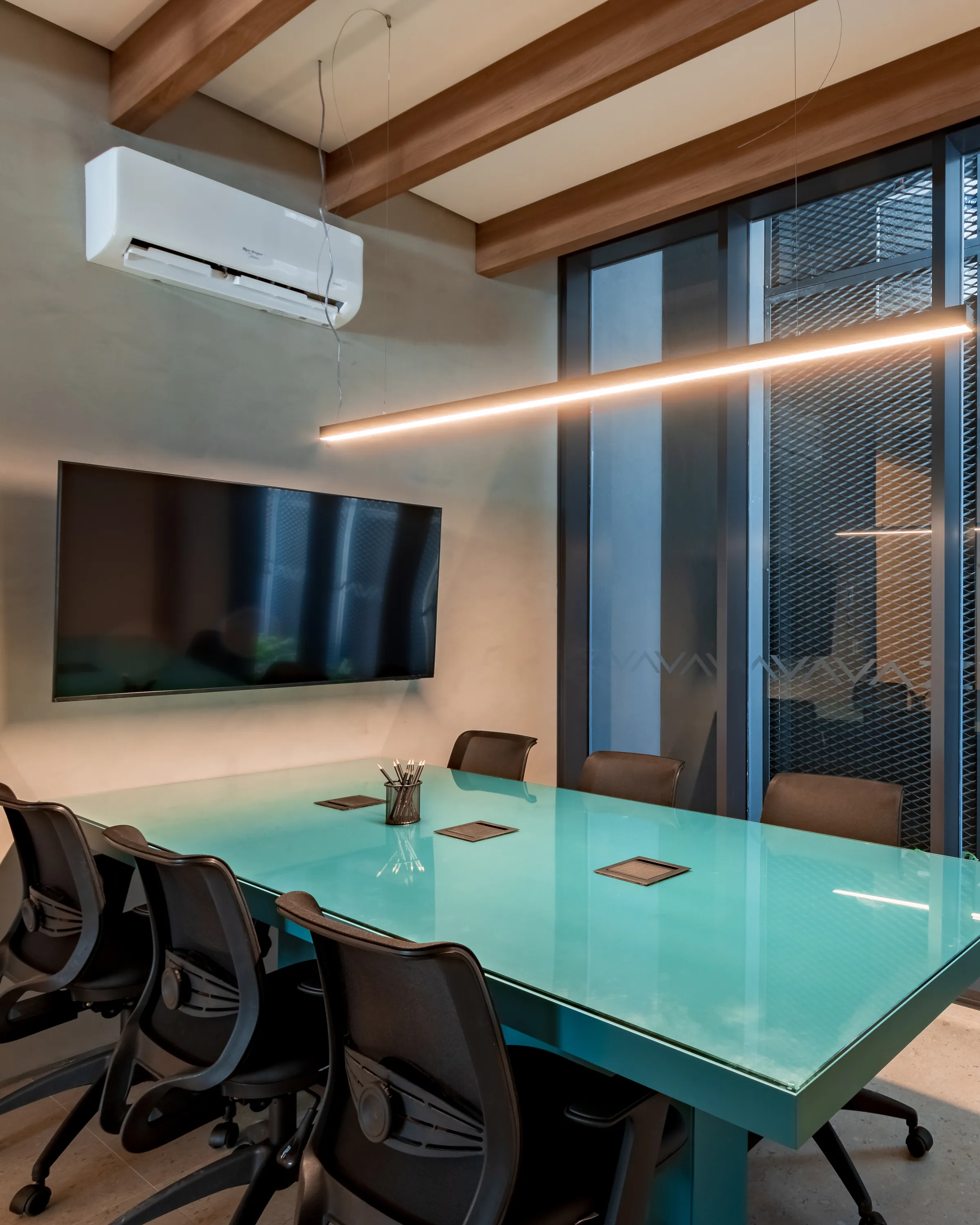 Sala de reuniões com mesa retangular em vidro azul-turquesa, cadeiras executivas pretas, TV de parede, luminária pendente linear e ar-condicionado split