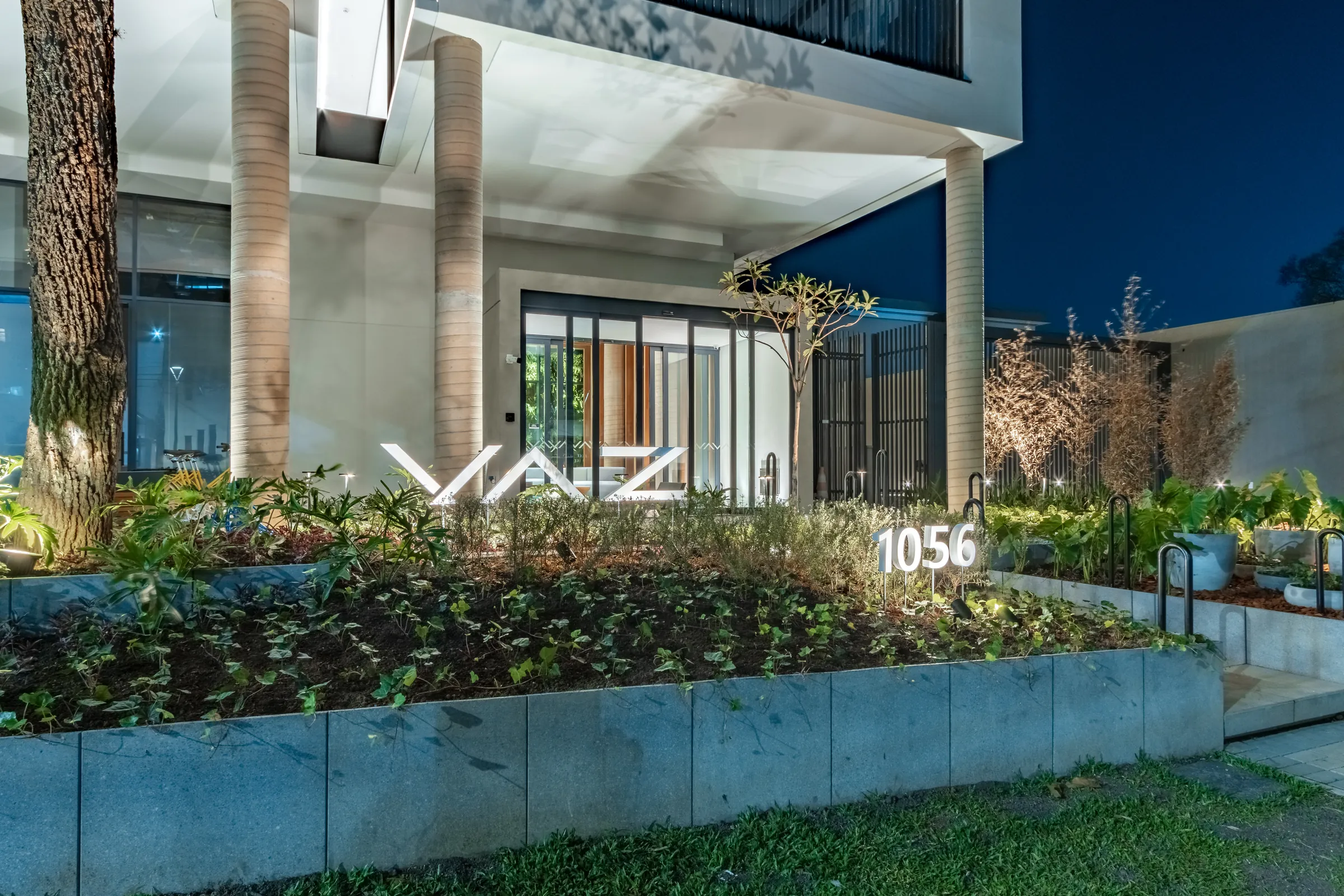 Entrada do Vaz Batel à noite com iluminação dourada, paisagismo e céu crepuscular